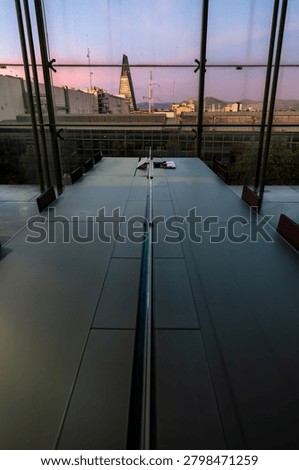 Interior view of a communal study table at the Vasconcelos Library with the Torre Insignia triangular skyscraper visible through the window at sunset, Mexico City, Mexico