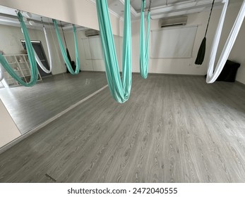 An interior view of an empty aerial yoga studio featuring hanging silk hammocks, mirrored walls, and wooden floor for exercises and stretching - Powered by Shutterstock