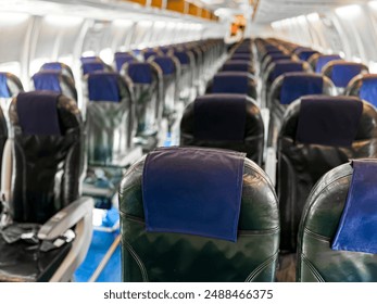 Interior view of empty airplane cabin with rows of black leather seats and blue headrest covers, illuminated by overhead lights, showing aisle running down middle and windows on both sides. - Powered by Shutterstock - Get 15% off with code: PIKWIZARD15