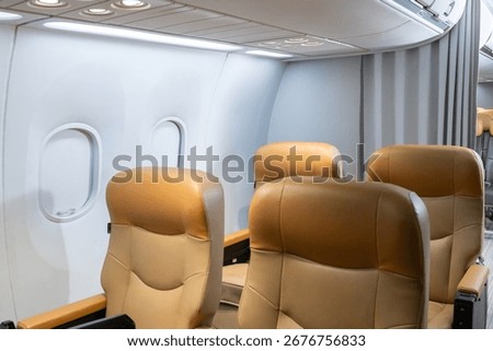 Interior view of empty airplane cabin featuring brown leather seats, closed overhead bins, and natural light through windows.