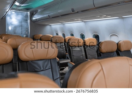Interior view of empty airplane cabin featuring brown leather seats, closed overhead bins, and natural light through windows.