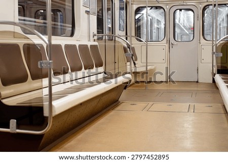Interior view of an empty classic underground metro train carriage with rows of vacant brown seats, metal handrails, and clean floor