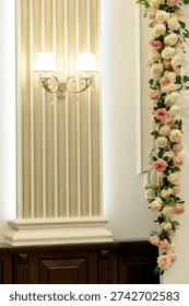 Interior view featuring a decorative wall with vertical paneling, wall sconces, and a floral arrangement of roses and greenery