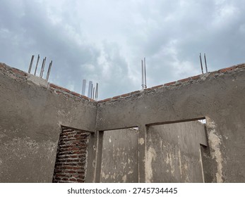 Interior view of a house under construction showing cement plastered walls, open doorway, and steel reinforcement bars against a cloudy sky