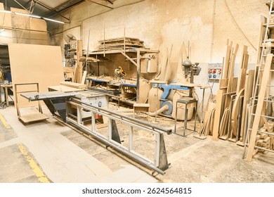 An interior view of a lumber workshop featuring various woodworking equipment, stacked wood, and tools. The organized space highlights industrial machinery and materials used in carpentry.