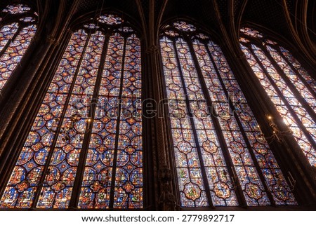 Interior view of medieval Gothic cathedral featuring towering stained-glass windows that fill nave with colored light, detailed biblical iconography. Medieval craftsmanship, advanced glazing technology.