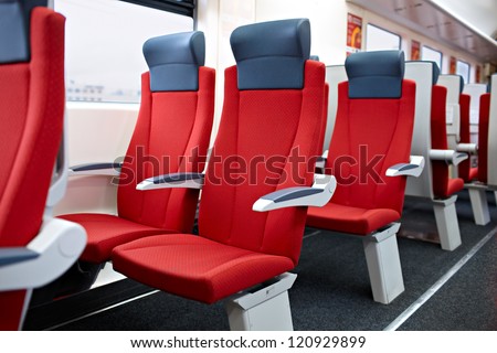 An interior view of  a modern high speed train. Red chairs.