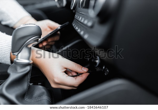 Interior view of a modern\
new car. Female model in the car charging her smartphone with usb\
power cord