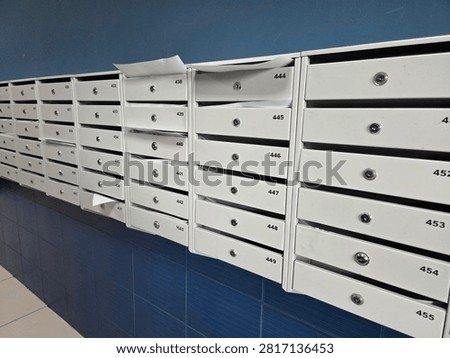 Interior view of numbered metal mailboxes mounted on a blue tiled wall in an apartment building lobby, some containing mail