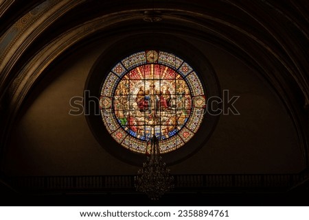 An interior view of an old church with a stained glass window of religious paintings