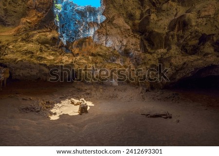 Interior view of Quadirikiri Caves in Aruba's national park, featuring an opening in the cave ceiling framing a view of the blue sky.