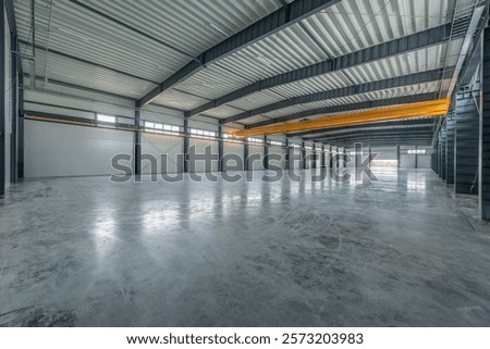 Interior view of a spacious, clean, and modern industrial warehouse with polished flooring and high ceilings, featuring bright natural lighting. Large Industrial Warehouse With Modern Design. Crane