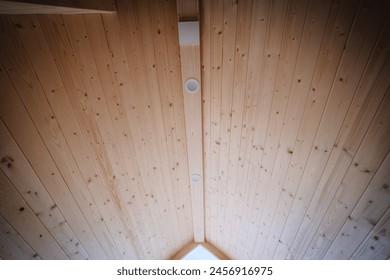 Interior view of a wooden cabin's ceiling featuring a sloped design with two embedded round lights and a symmetric wooden beam structure. - Powered by Shutterstock