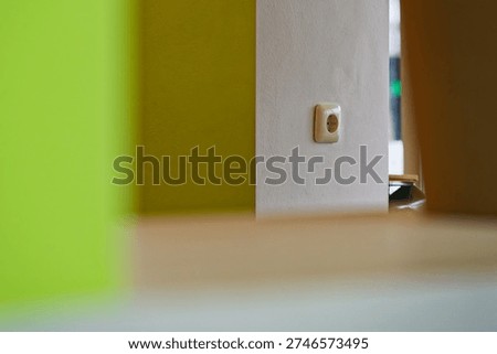 Interior wall featuring a white electrical outlet surrounded by green and white painted surfaces, showcasing a minimalist and modern design.