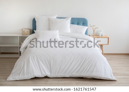 Interior with white bed linen on the sofa. Bedroom with bed, white bedding, and bedside table. White pillows, duvet and duvet case on bed with blue headboard. Front view.