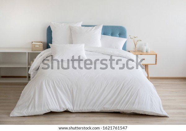 Interior with white bed linen\
on the sofa. Bedroom with bed, white bedding, and bedside table.\
White pillows, duvet and duvet case on bed with blue headboard.\
Front view.