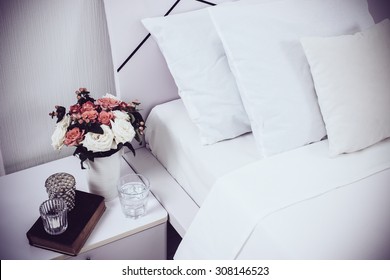 Interior Of White Bedroom, New Linens On The Bed, The Room At The Hotel. Bedside Table Decor And Pillows Closeup.