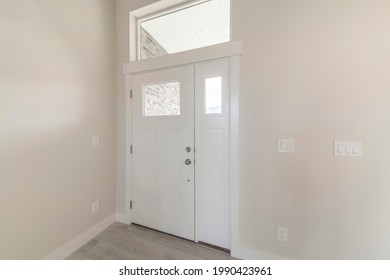 Interior Of A White Wooden Front Door With Side Panel And Top Transom Window. Entrance Of A House With Electrical Light Switch And Plugs On A Wall, And A View Of Brick Wall Outside.