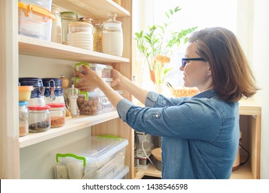 Interior of wooden pantry with products for cooking. Adult woman taking kitchenware and food from the shelves. - Shutterstock ID 1438546598