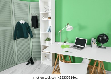 Interior of workplace with desk, shelving unit, laptop computer, shoes and stylish school uniform hanging on folding screen - Shutterstock ID 2330532461