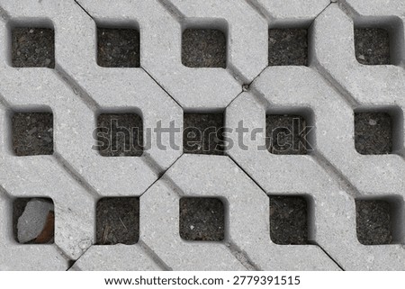 Interlocking concrete modules form a structured lattice, protecting soil beneath while allowing sparse greenery to emerge. The image conveys a balance between industrial rigidity and organic life, evo