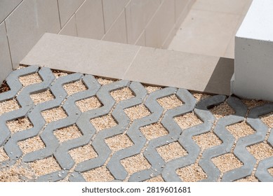 Interlocking concrete pavers with a geometric pattern are filled with small beige gravel for a permeable surface