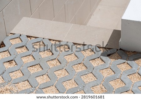 Interlocking concrete pavers with a geometric pattern are filled with small beige gravel for a permeable surface