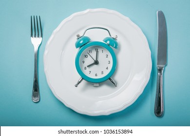 Intermittent fastin concept - empty plate on blue background