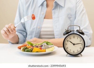 Intermittent fasting with clock, close up young woman, girl diet, waiting time to eat ketogenic low carb, green vegetable salad on plate. Eat food healthy first meal on brunch, lunch on table at home. - Powered by Shutterstock