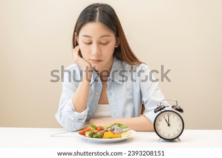 Intermittent fasting with clock, close up young woman, girl diet, waiting time to eat ketogenic low carb, green vegetable salad on plate. Eat food healthy first meal on brunch, lunch on table at home.