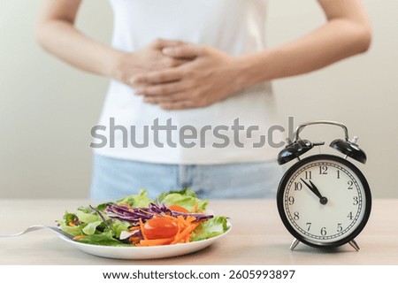 Intermittent fasting with clock, close up young woman, girl diet, waiting time to eat ketogenic low carb, green vegetable salad on plate. Eat food healthy first meal on brunch, lunch on table at home.