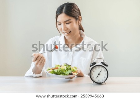 Intermittent fasting concept, close up clock, asain young woman, girl diet eating ketogenic low carb, fresh green vegetable salad on plate. Eat food healthy first meal in morning on table at home.