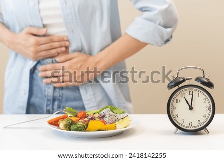 Intermittent fasting, diet healthy asian young woman dietary, having stomach ache, temptation hungry of brunch food in morning on table at home, waiting time to eat salad but not yet time first meal.