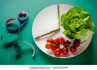 Intermittent Fasting Diet Method - Sixteen Hours Diet, Eight Hours Eating Time. White Plate As Clock With Vegetables And Centimeter Tape On Green Background. Weight Loss And Healthy Lifestyle.