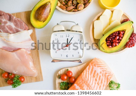  Intermittent fasting and Healthy food. Concept.Alarm clock and Keto diet food ingredients on white table.Ketogenic mean Low carb and High fat.