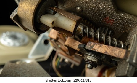 Internal Mechanism Of An Old Disassembled Rotary Telephone. Threaded Metal Screws, Nuts, Gears, Dusty Plastic Parts. A Macro Shot Of The Details Of A Broken Vintage Landline Phone. Repair In Workshop.