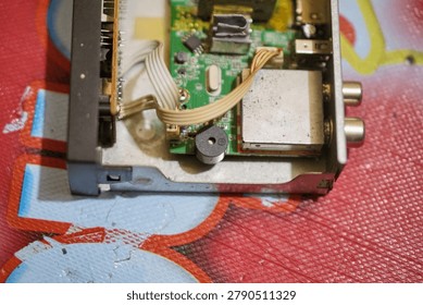 Internal view of disassembled electronic components, showing a green circuit board, yellow transformer, ribbon cable, and metal tuner module.