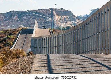 The international border wall between San Diego, California and Tijuana, Mexico, with an approaching Border Patrol vehicle on a nearby hill.  - Shutterstock ID 753020731
