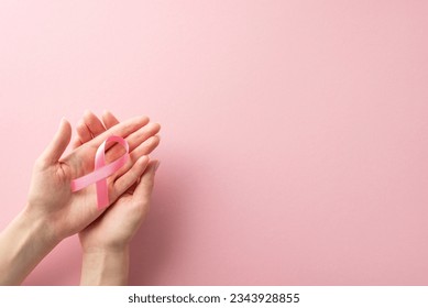 International Breast Cancer Awareness Month concept. High-angle view photo of woman's hands holding pink ribbon on pastel pink isolated background with copyspace for text or advertising