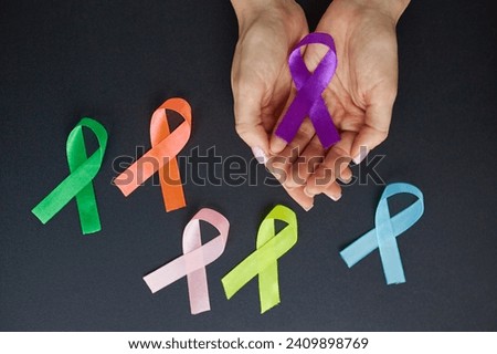 International Breast Cancer Awareness Month concept. Woman's hands holding violet ribbon on dark isolated background with copyspace for text or advertising