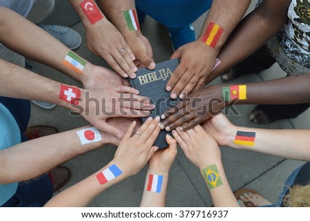 International brothers and sisters in Christ with different flags painted on their arms holding a bible together.