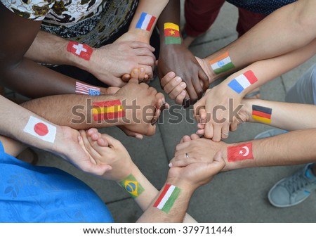 International brothers and sisters with different flags painted on their arms standing in a circle together and holding hands.