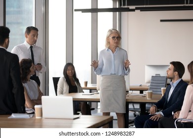 International Company Members Diverse Staff Listen Aged Attractive Serious Coach Gathered Together In Morning At Contemporary Coworking Space. Executive Manager Telling About New Project At Briefing