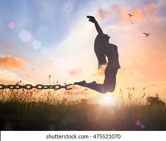 International day for the remembrance of the slave trade and its abolition concept: Silhouette of a woman jumping and broken chains at orange meadow autumn sunset with her hands raised
