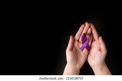 International Epilepsy Day. Adult Hands Holding Purple Ribbon On Black Background. Alzheimer's Disease, Pancreatic Cancer, Hodgkin's Lymphoma Awareness