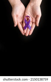 International Epilepsy Day. Adult Hands Holding Purple Ribbon On Black Background. Alzheimer's Disease, Pancreatic Cancer, Hodgkin's Lymphoma Awareness