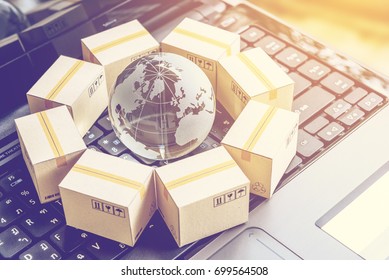 International freight or shipping service for online shopping or ecommerce concept : Paper boxes or carton put in circle around a clear crystal globe with world map on a computer notebook keyboard.
