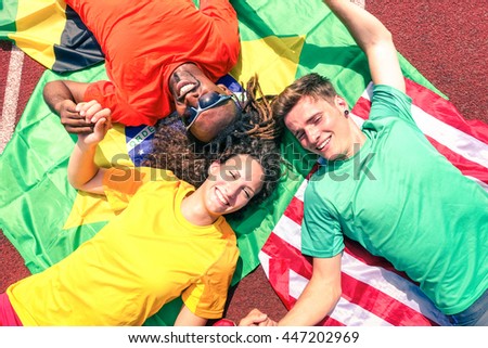 International friends of sport fans circle looking up at  sky - Cheerful multiracial athletes lying on national flags after competition at stadium athletic track -  Multinational friendship concept