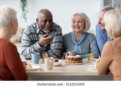 International group of positive men and women sitting around table drinking tea with cake and having conversation, smiling and laughing, having home party or enjoying time at nursing home - Powered by Shutterstock