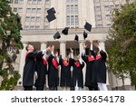 International group of students standing in a row and throwing graduation caps up in the air, posing next to university building after graduation ceremony, celebrating freedom